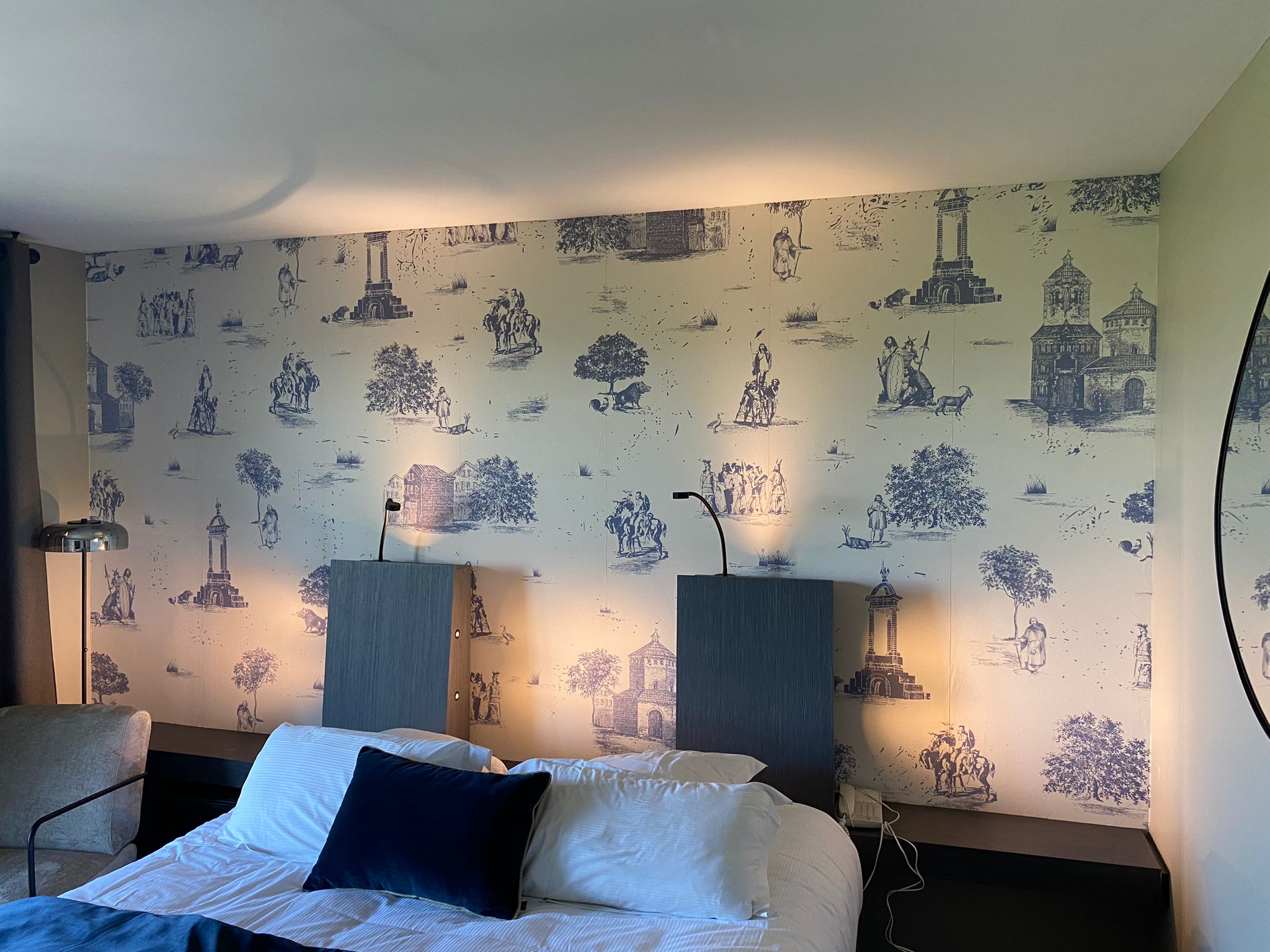 Papier peint à motif décoratif dans une chambre, présentant des motifs géométriques (ou floraux, abstraits, etc. — à adapter selon l’image), dans des tons doux et apaisants, posé sur un mur derrière un lit pour une ambiance élégante et chaleureuse.